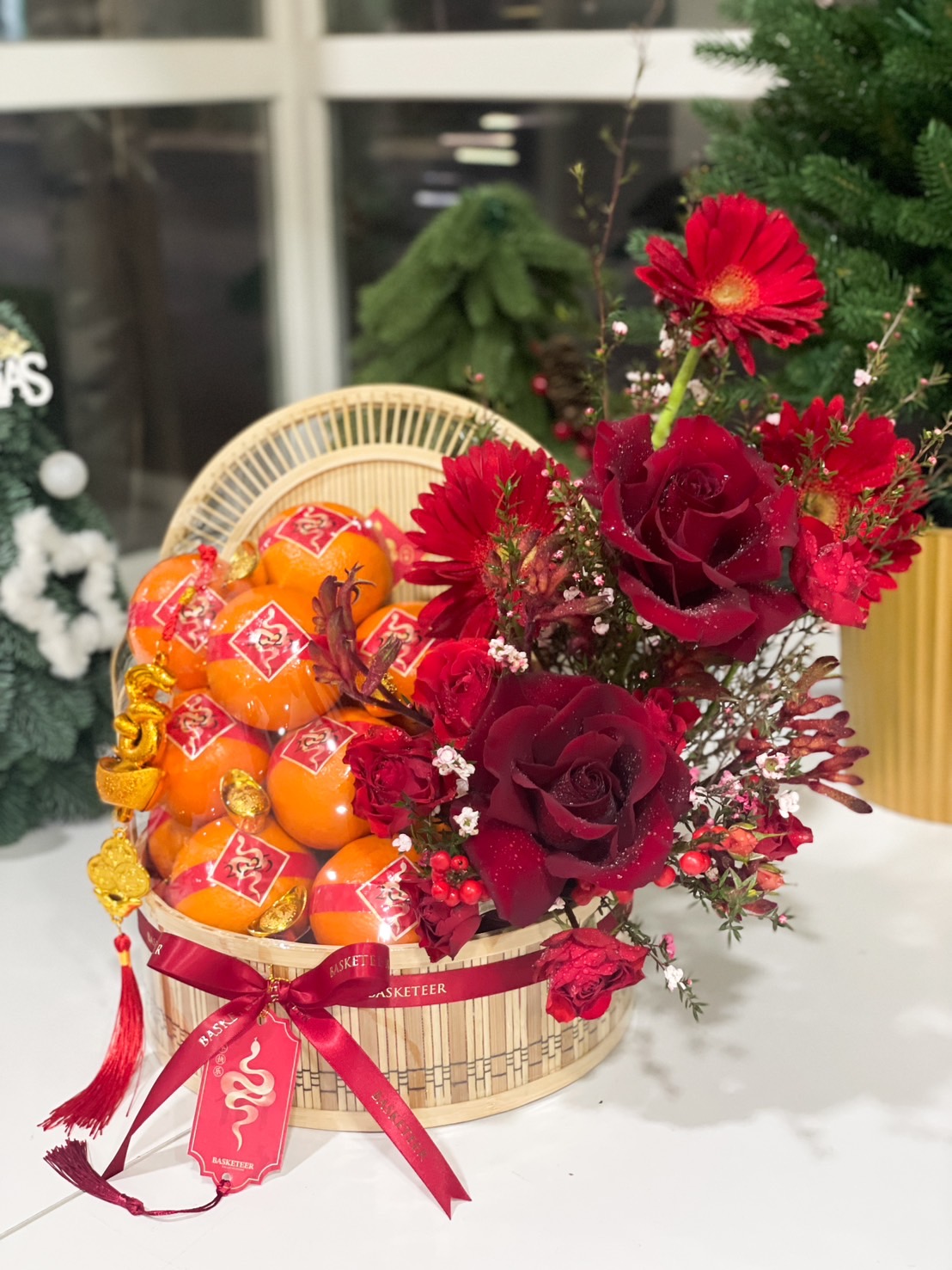 A bamboo basket decorated with fresh mandarins, red roses, and festive ornaments, perfect for Chinese New Year celebrations.