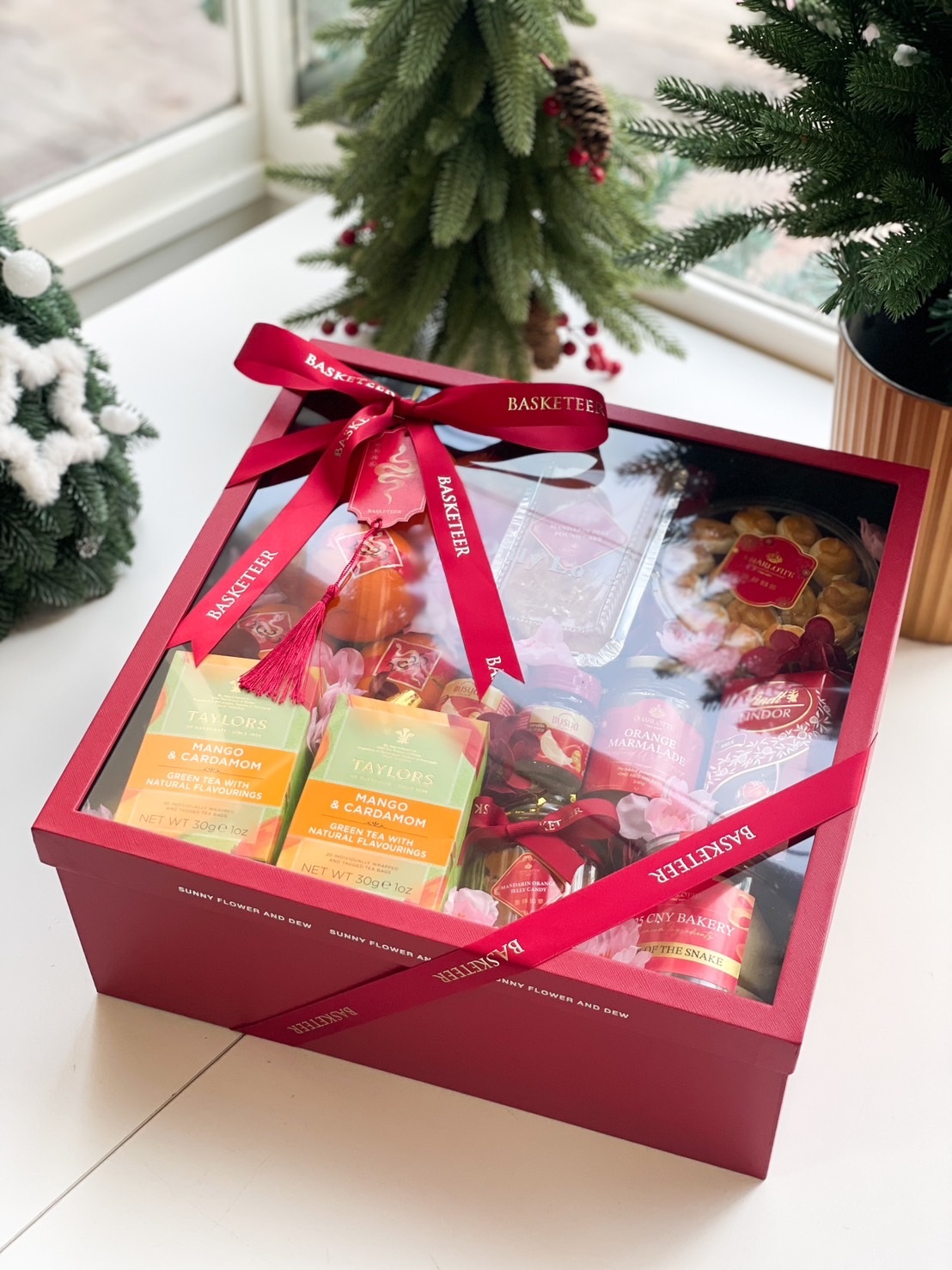 Red deluxe gift hamper with Taylors Mango & Cardamom tea, orange marmalade, festive cookies, and vibrant floral accents.