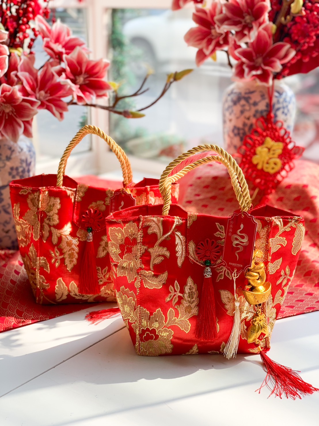 Luxury red silk gift bag with gold embroidery, decorative tassels, and lucky charms, set in a festive Chinese New Year display.