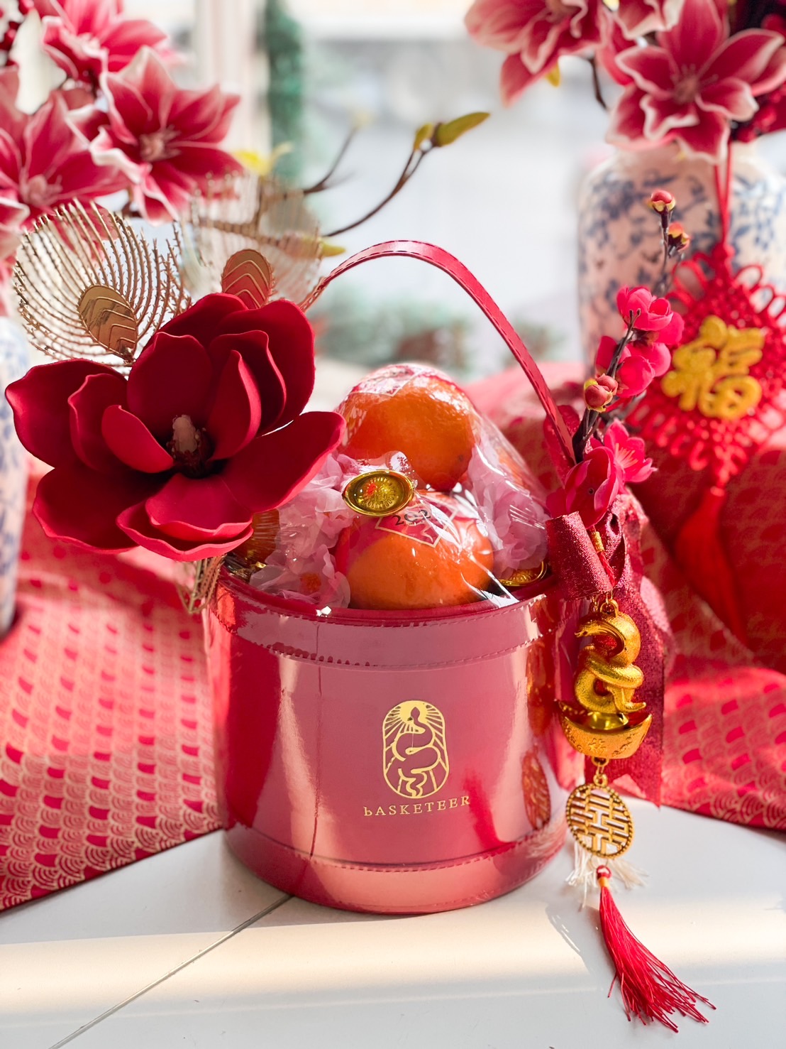 Red luxury Chinese New Year gift basket with oranges, decorative flowers, and gold accents, perfect for festive celebrations.