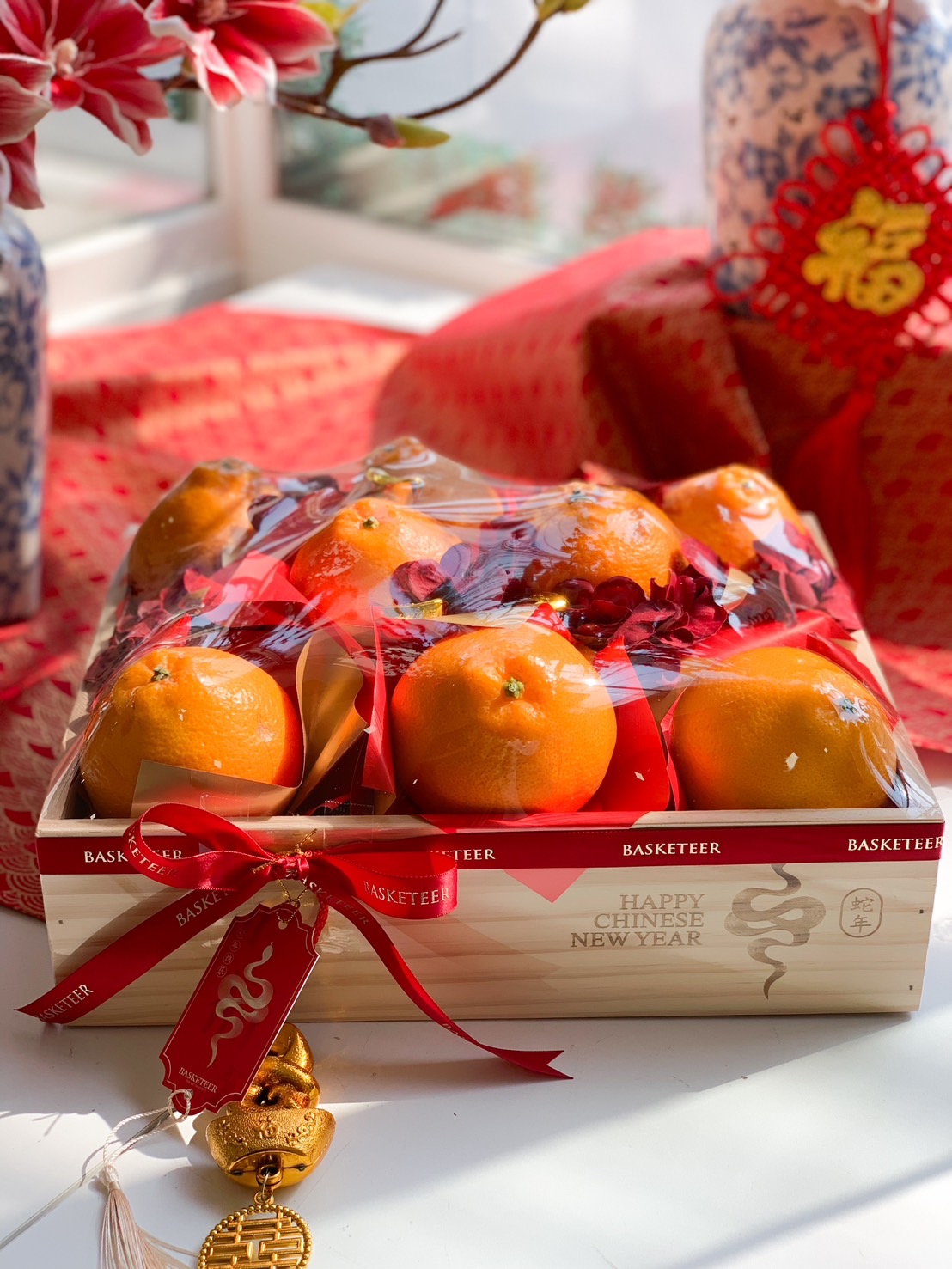 Chinese New Year wooden fruit box with fresh Mandarin oranges, red ribbons, and gold prosperity charms for a festive and elegant celebration.