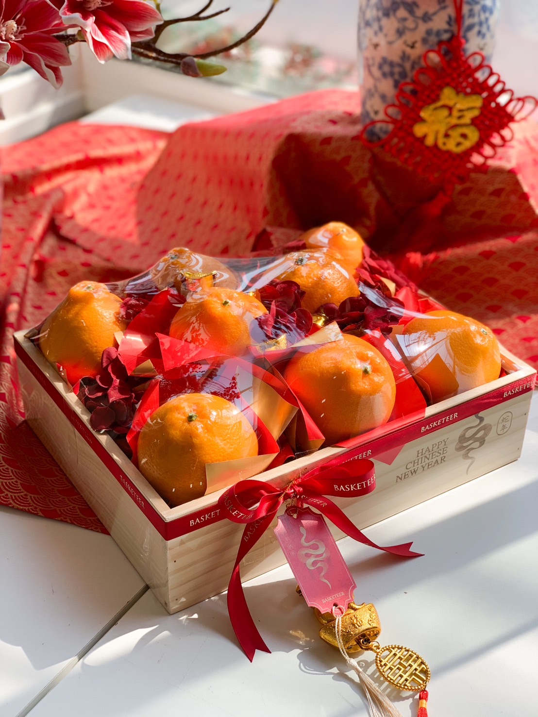 Chinese New Year wooden fruit box with fresh Mandarin oranges, red ribbons, and gold prosperity charms for a festive and elegant celebration.