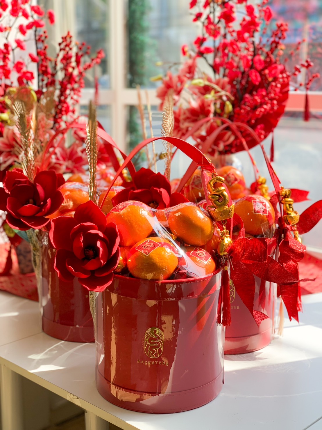 Luxury Chinese New Year Mandarin orange gift basket with fresh fruit, red floral decorations, and gold prosperity charms for festive gifting.