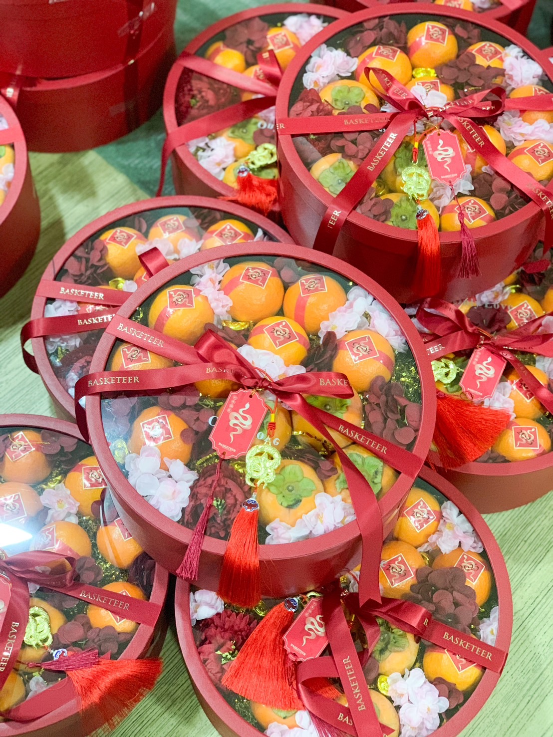 Premium Chinese New Year round gift box set with Mandarin oranges, decorative flowers, and festive red ribbons, symbolizing prosperity and fortune.