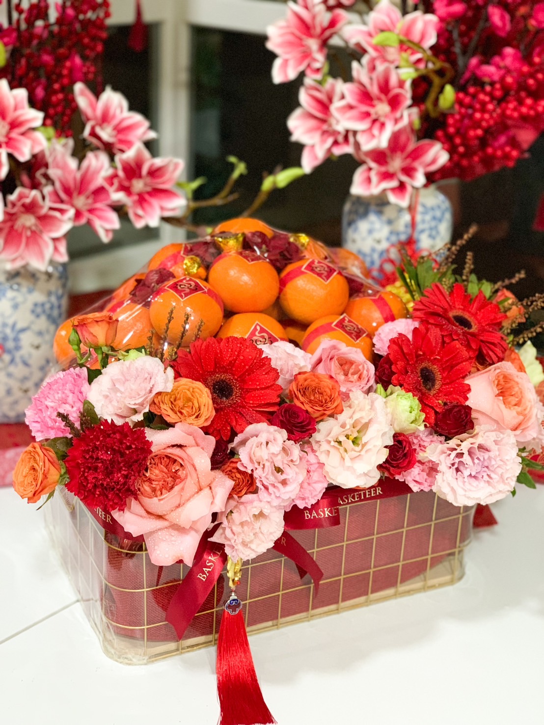 Chinese New Year gift basket with premium Mandarin oranges, vibrant red and pink flowers, and festive decorations for a prosperous celebration.