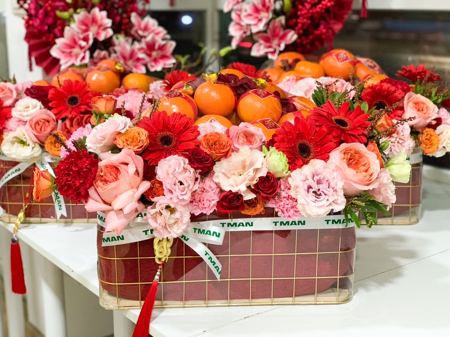 Chinese New Year gift basket with fresh Mandarin oranges and red and pink floral arrangements, symbolizing prosperity and good fortune.