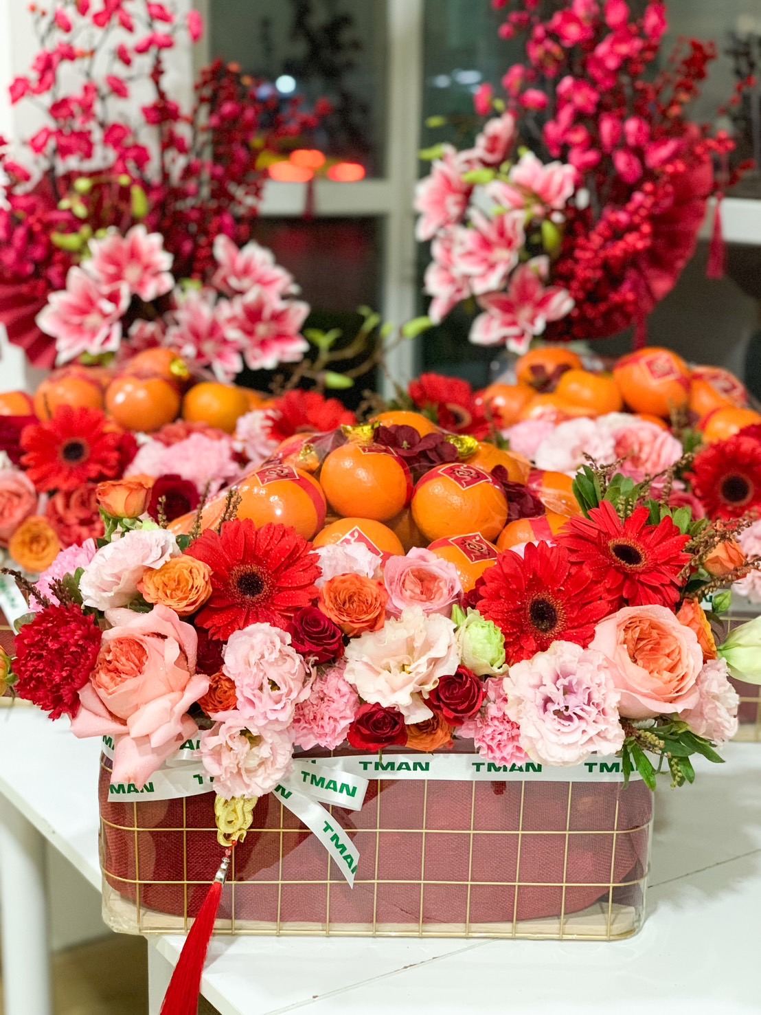Chinese New Year gift basket with fresh Mandarin oranges and red and pink floral arrangements, symbolizing prosperity and good fortune.