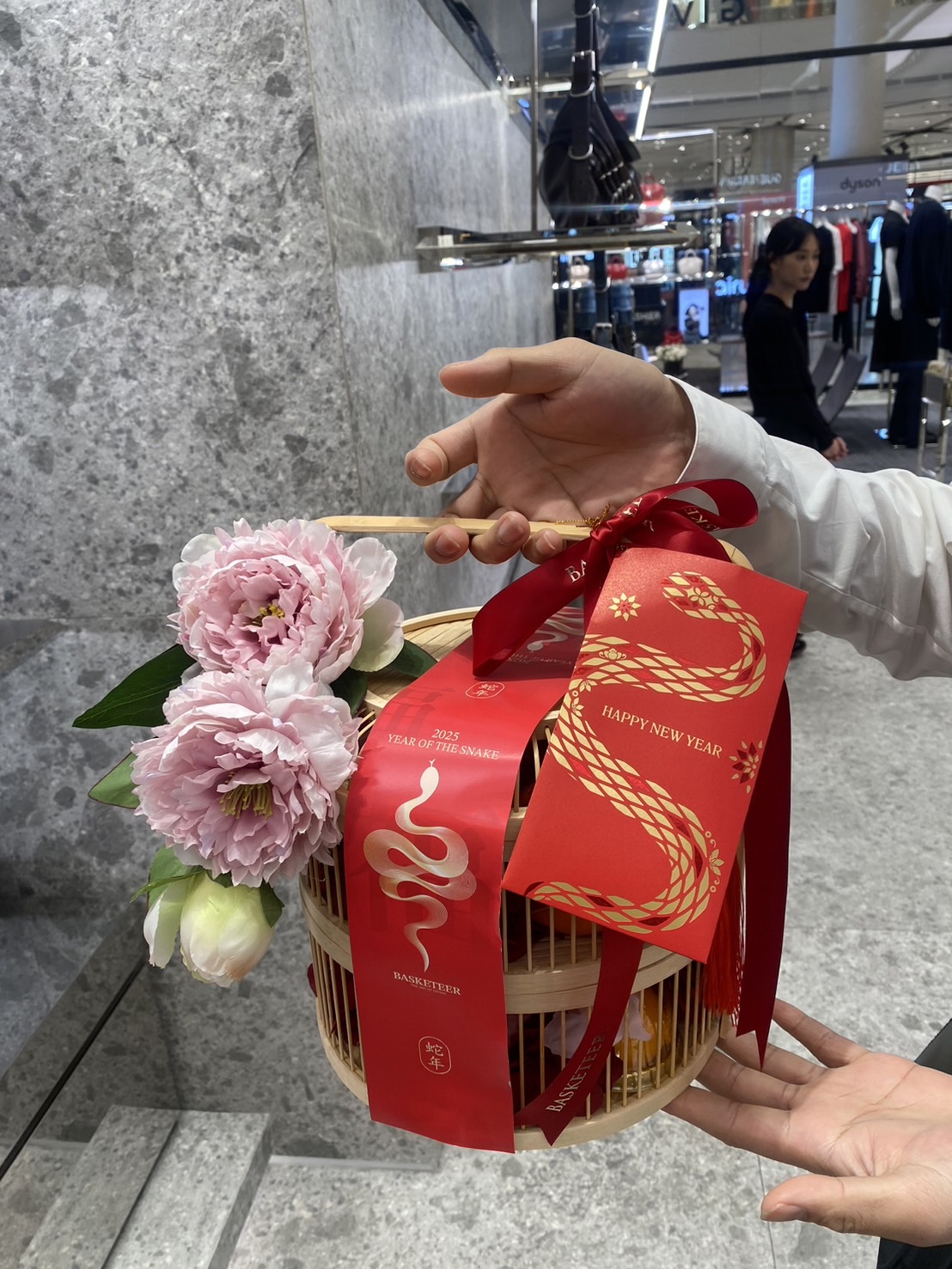 Traditional bamboo Chinese New Year gift basket with pink peonies, red ribbons, and gold accents for prosperity and good luck.