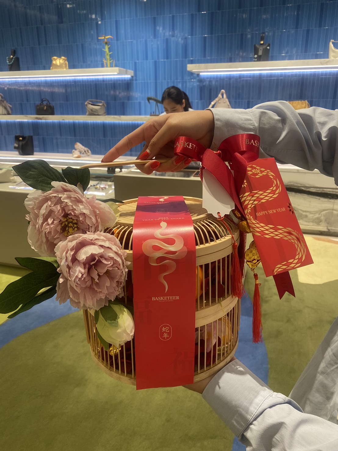 Traditional bamboo Chinese New Year gift basket with pink peonies, red ribbons, and gold accents for prosperity and good luck.