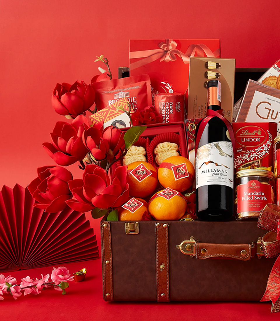 Close-up of a Luxury Chinese New Year gift hamper in a vintage-style trunk, filled with premium wine, chocolates, cookies, mandarin oranges, and gourmet treats, elegantly decorated with red floral accents and festive ribbons.