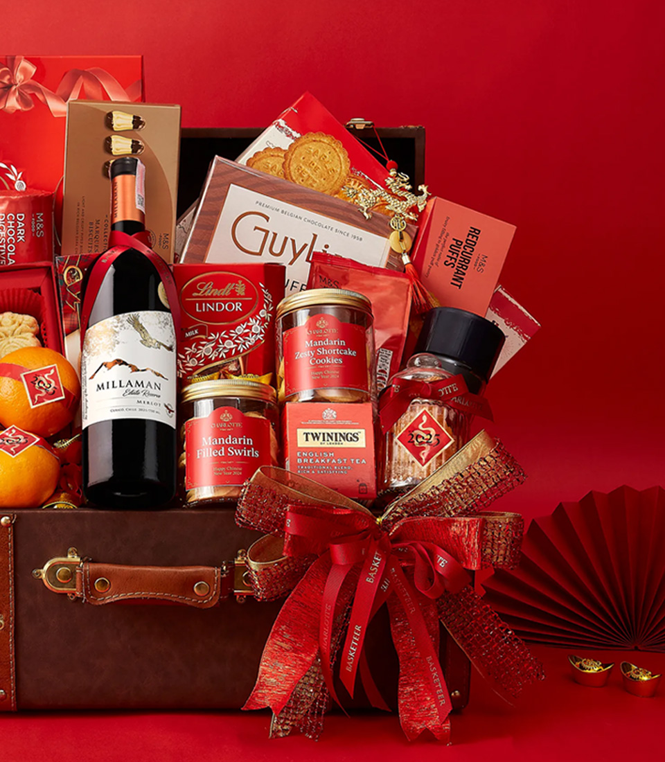 Close-up of a Luxury Chinese New Year gift hamper in a vintage-style trunk, filled with premium wine, chocolates, cookies, mandarin oranges, and gourmet treats, elegantly decorated with red floral accents and festive ribbons.
