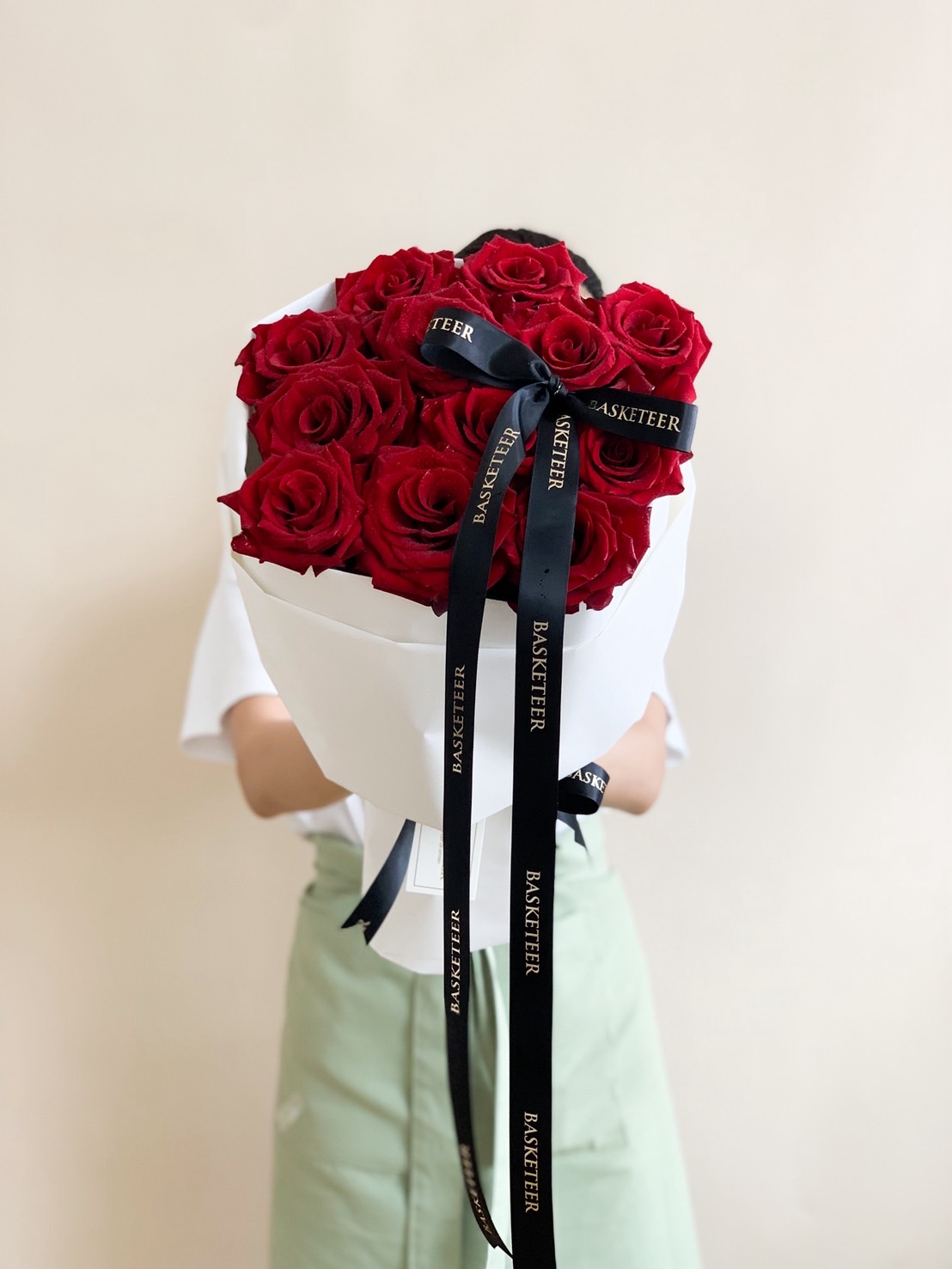Elegant bouquet of premium red roses wrapped in white paper with a black Basketeer ribbon.
