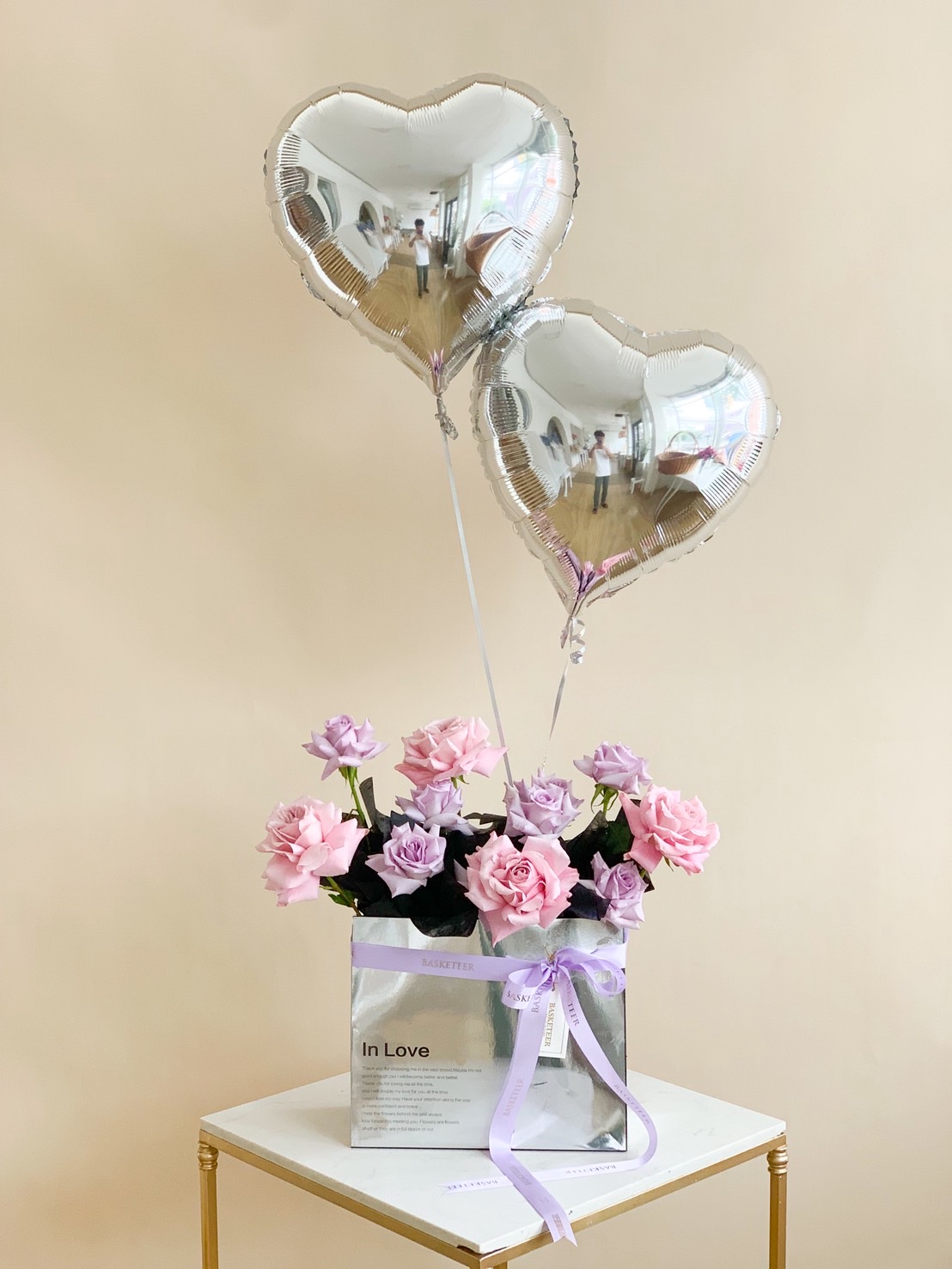 Arrangement of pink and purple roses in silver box with silver heart balloons.