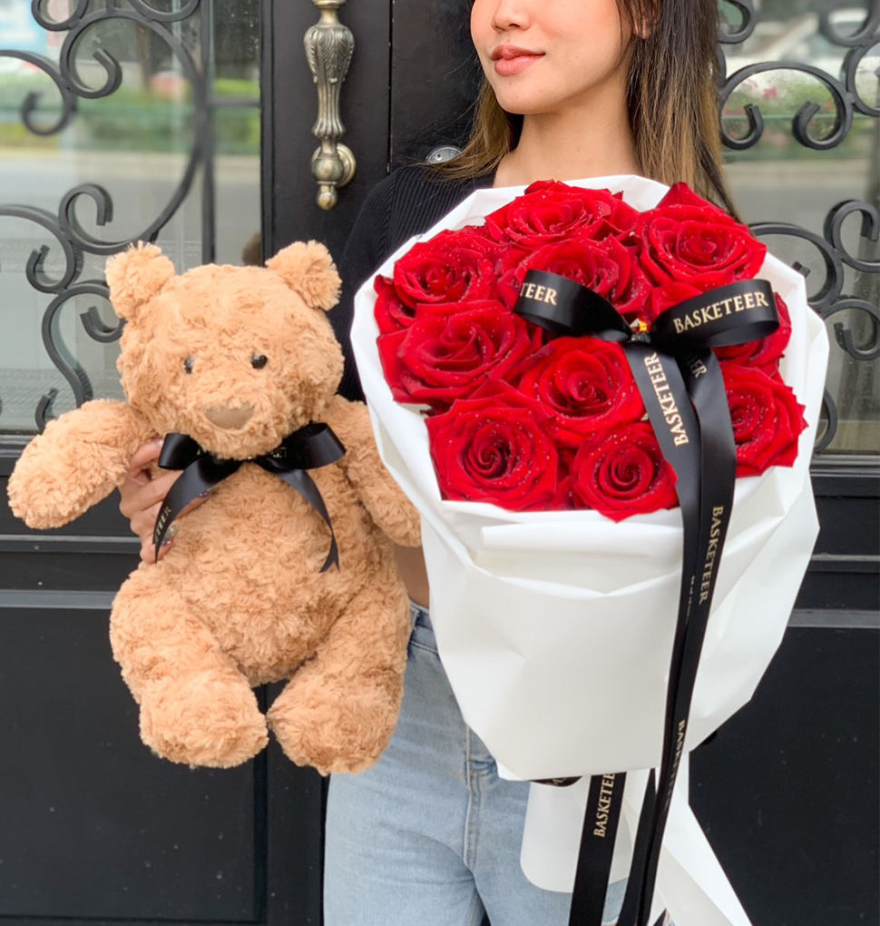 A luxurious hand-tied bouquet of deep red roses, wrapped in elegant white paper with black ribbons, creating a romantic and sophisticated floral arrangement.