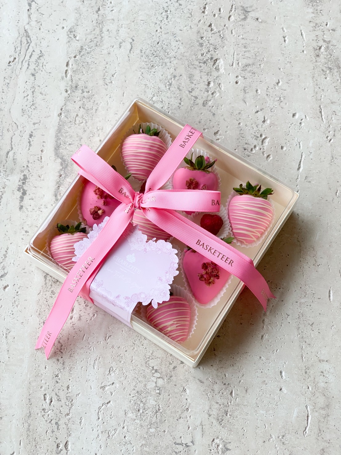 Gift box of pink chocolate dipped strawberries decorated with pink ribbons and dried rose petals.
