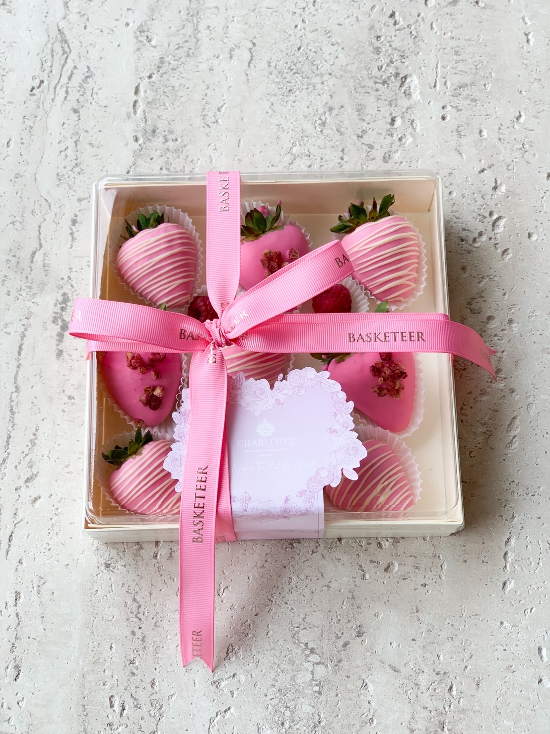 Elegant gift box of pink chocolate covered strawberries decorated with pink ribbons and rose petals.