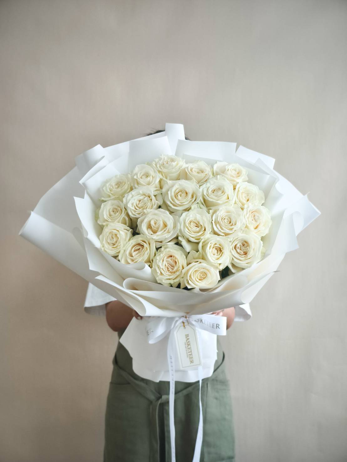 Elegant bouquet of fresh white roses wrapped in chic white paper and ribbon, luxury flower gift.