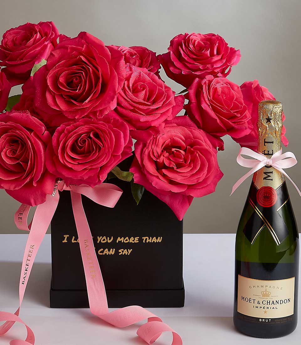 A black box with vibrant red roses and a pink ribbon with gold text stating 