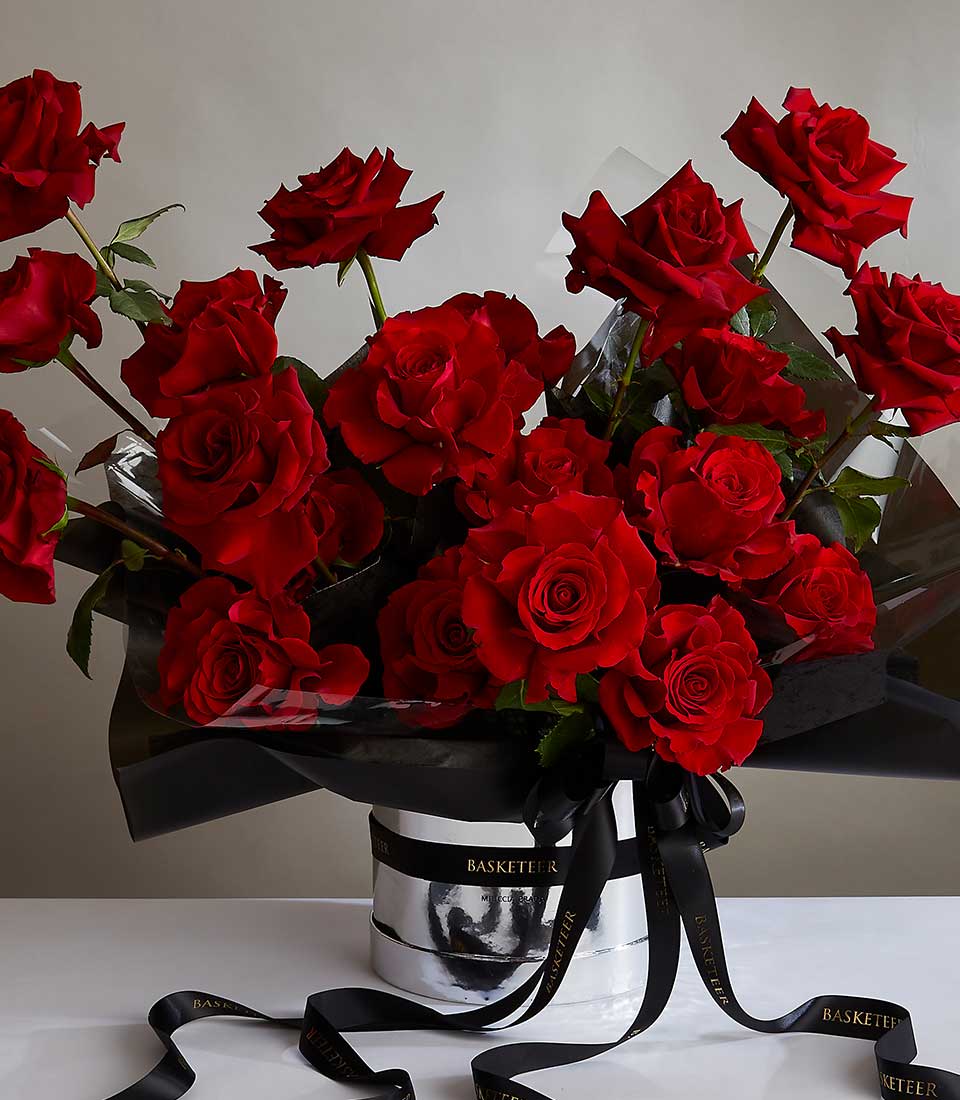 A luxurious bouquet of vibrant red roses arranged in a white marble-patterned vase adorned with 