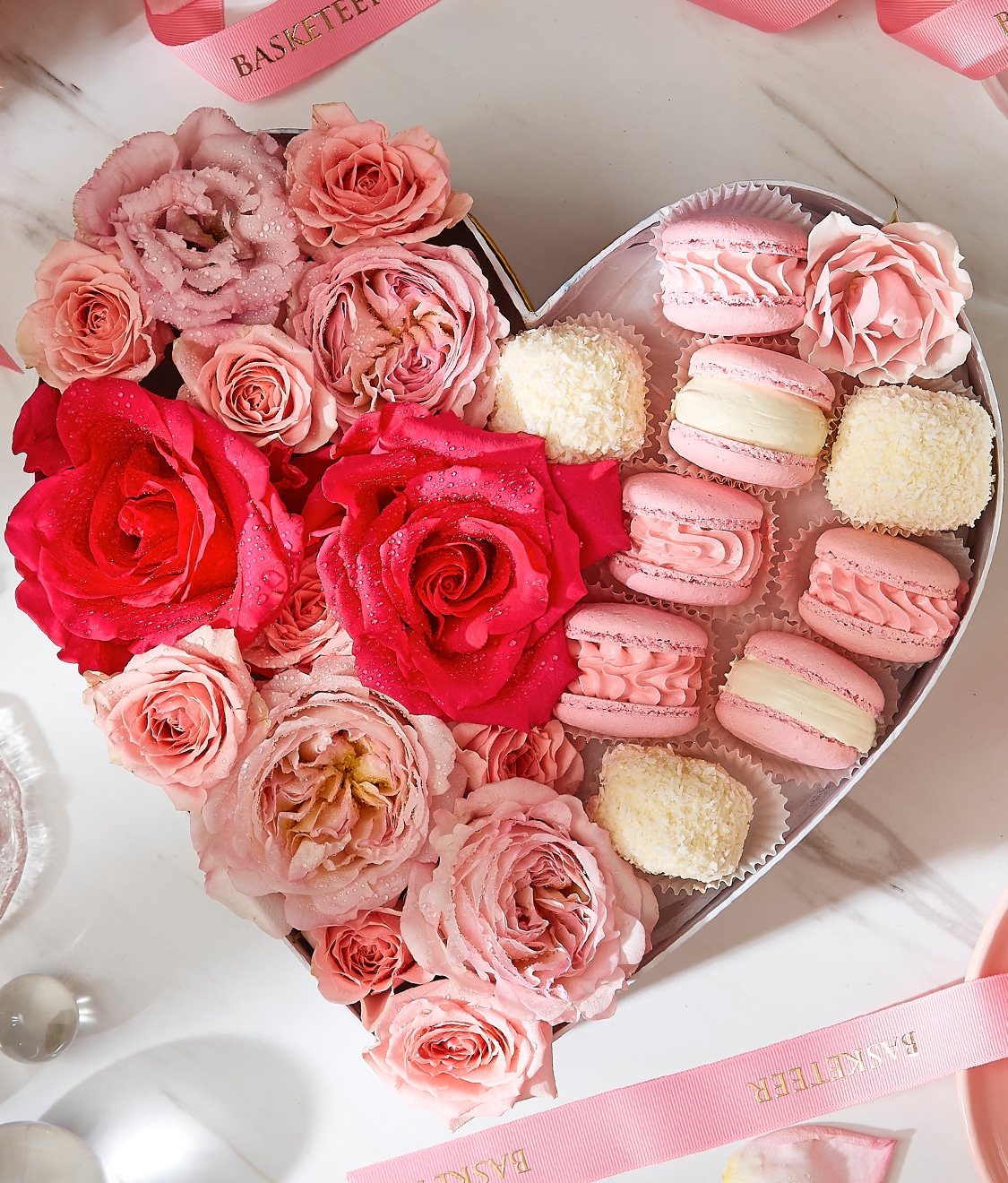Sweet pink macarons in heart-shaped box with pink flower decorations.