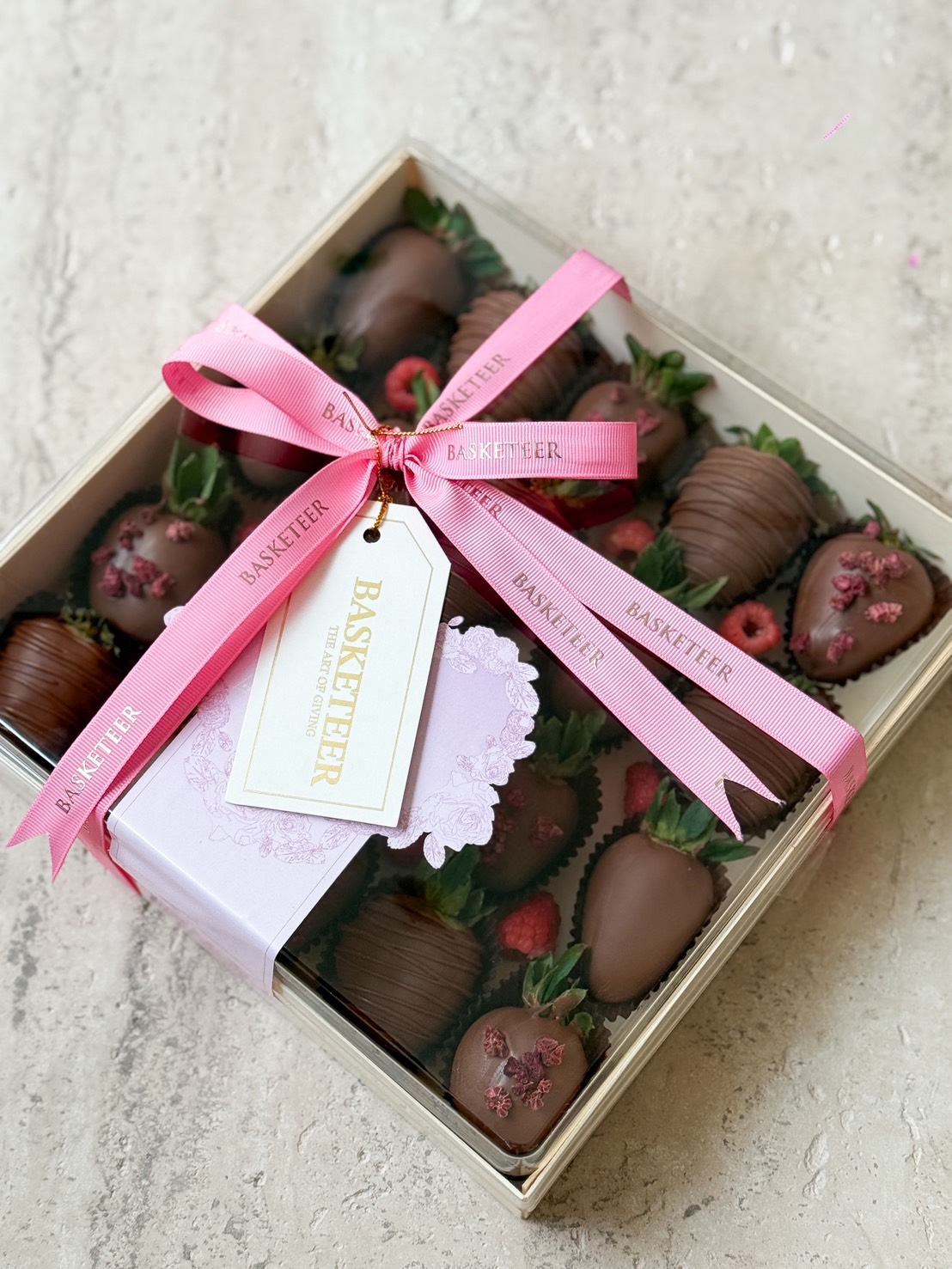 A luxurious Basketeer chocolate-covered strawberries gift box with pink ribbon and raspberry-topped berries, perfect for Bangkok gifting.