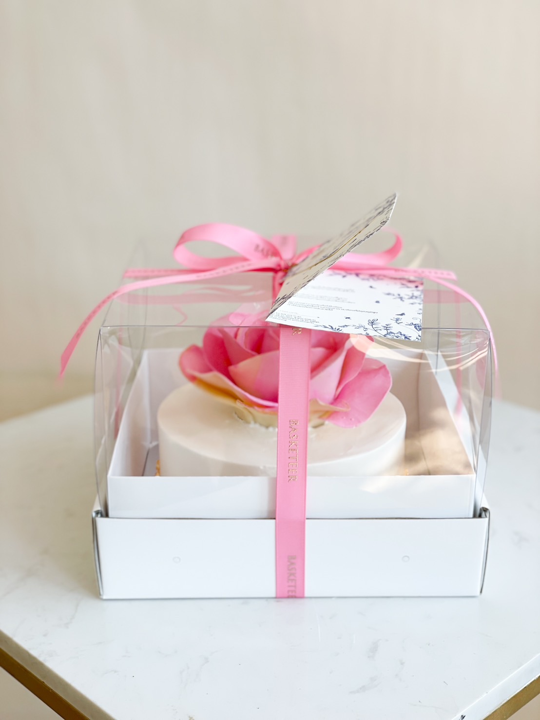Luxury pink rose cake in a transparent gift box with a pink ribbon, perfect for special occasions.