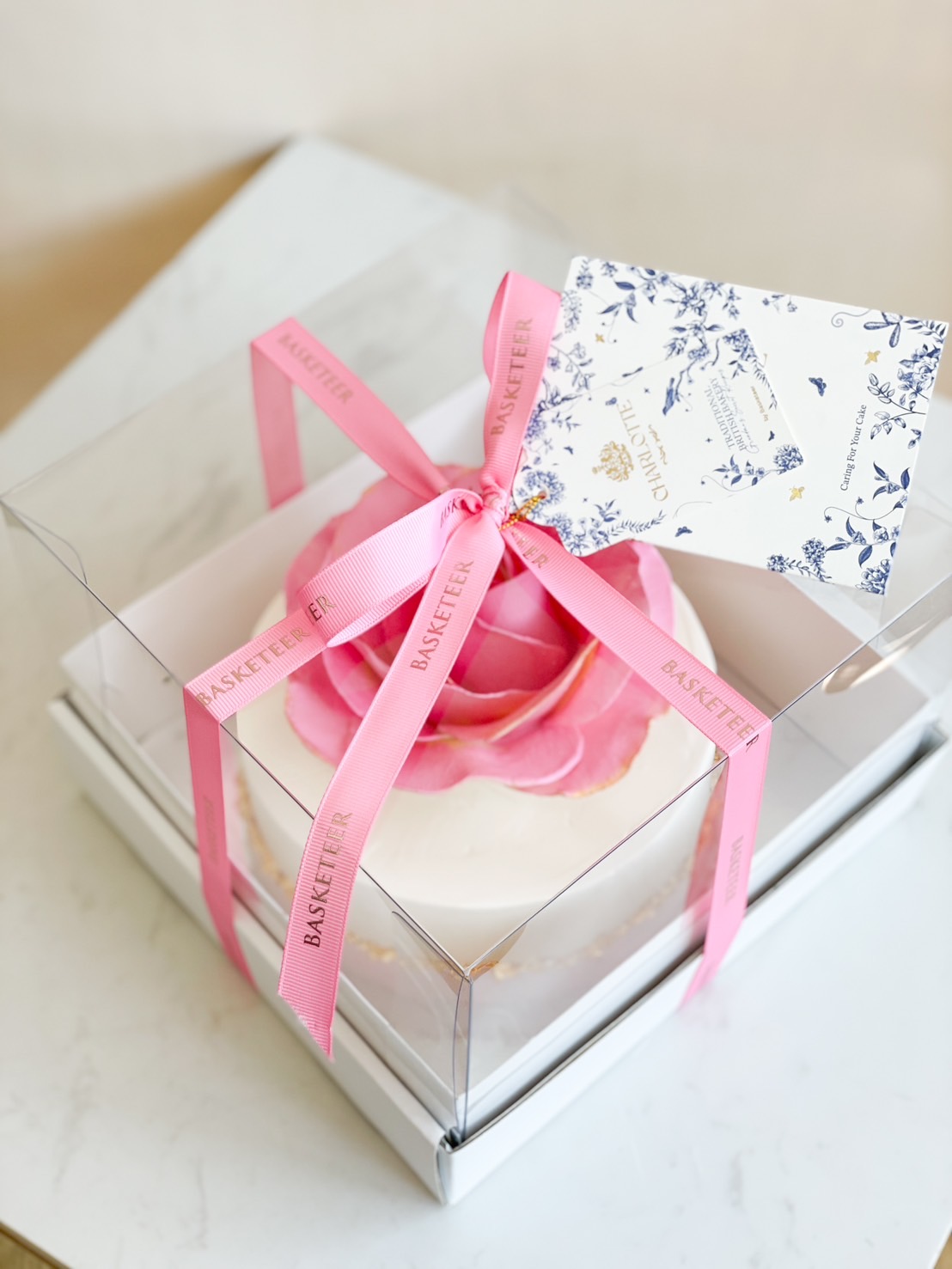 Luxury pink rose cake in a transparent gift box with a pink ribbon, perfect for special occasions.