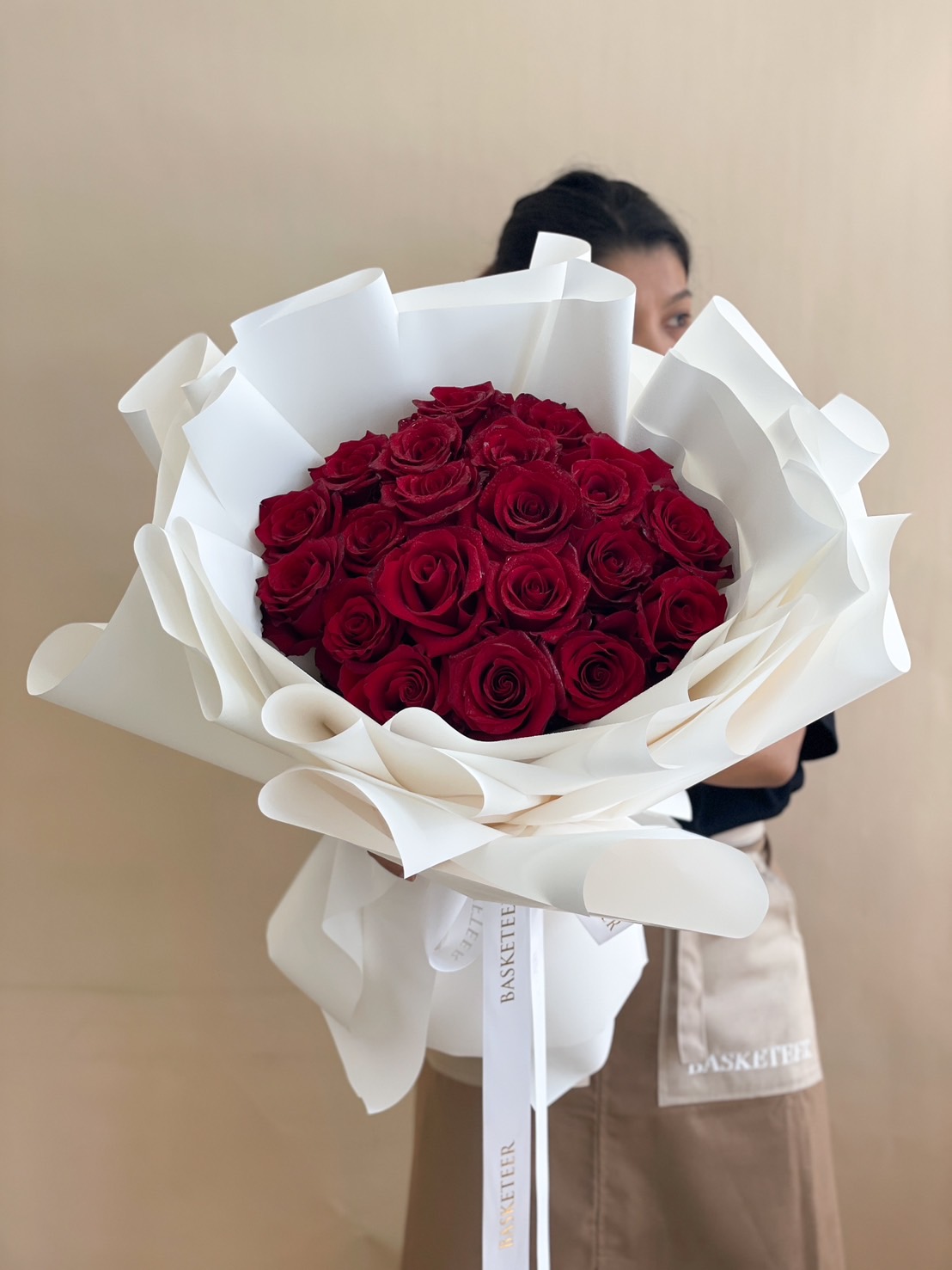 A luxurious hand-tied bouquet of premium red roses, elegantly wrapped in white paper with a Basketeer ribbon.