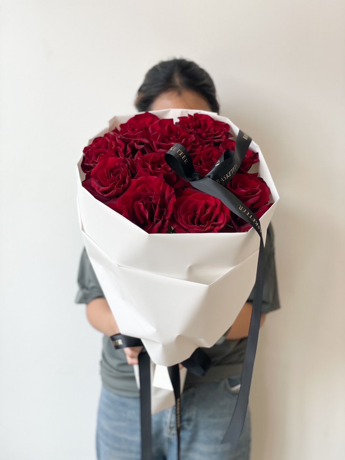A luxurious hand-tied bouquet of deep red roses, wrapped in elegant white paper with black ribbons, creating a romantic and sophisticated floral arrangement.