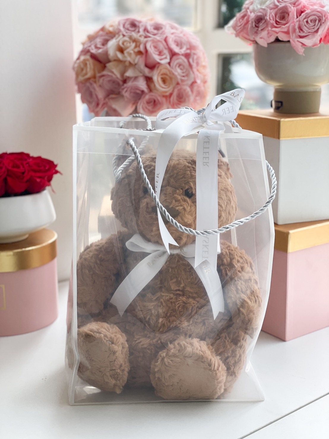 A soft brown plush teddy bear elegantly packaged in a luxury sheer gift bag with a white ribbon, perfect for a romantic or thoughtful gift.