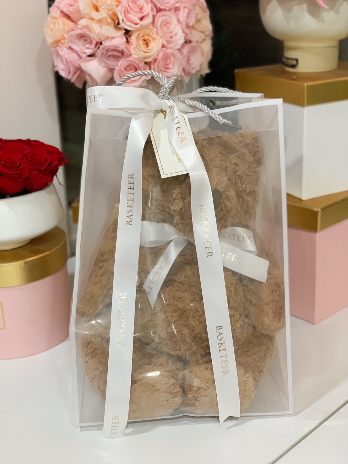 A soft brown plush teddy bear elegantly packaged in a luxury sheer gift bag with a white ribbon, perfect for a romantic or thoughtful gift.
