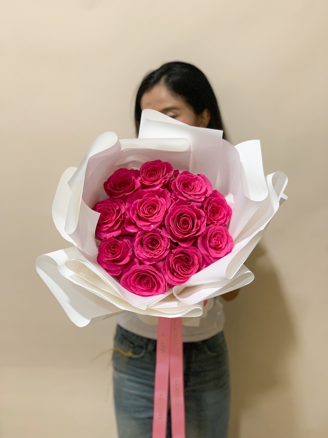 A stunning fuchsia pink garden rose bouquet, elegantly wrapped in crisp white paper, tied with a delicate pink ribbon, making it a perfect luxury floral gift.