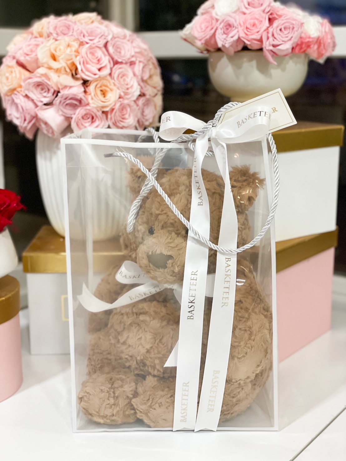 A soft brown plush teddy bear elegantly packaged in a luxury sheer gift bag with a white ribbon, perfect for a romantic or thoughtful gift.