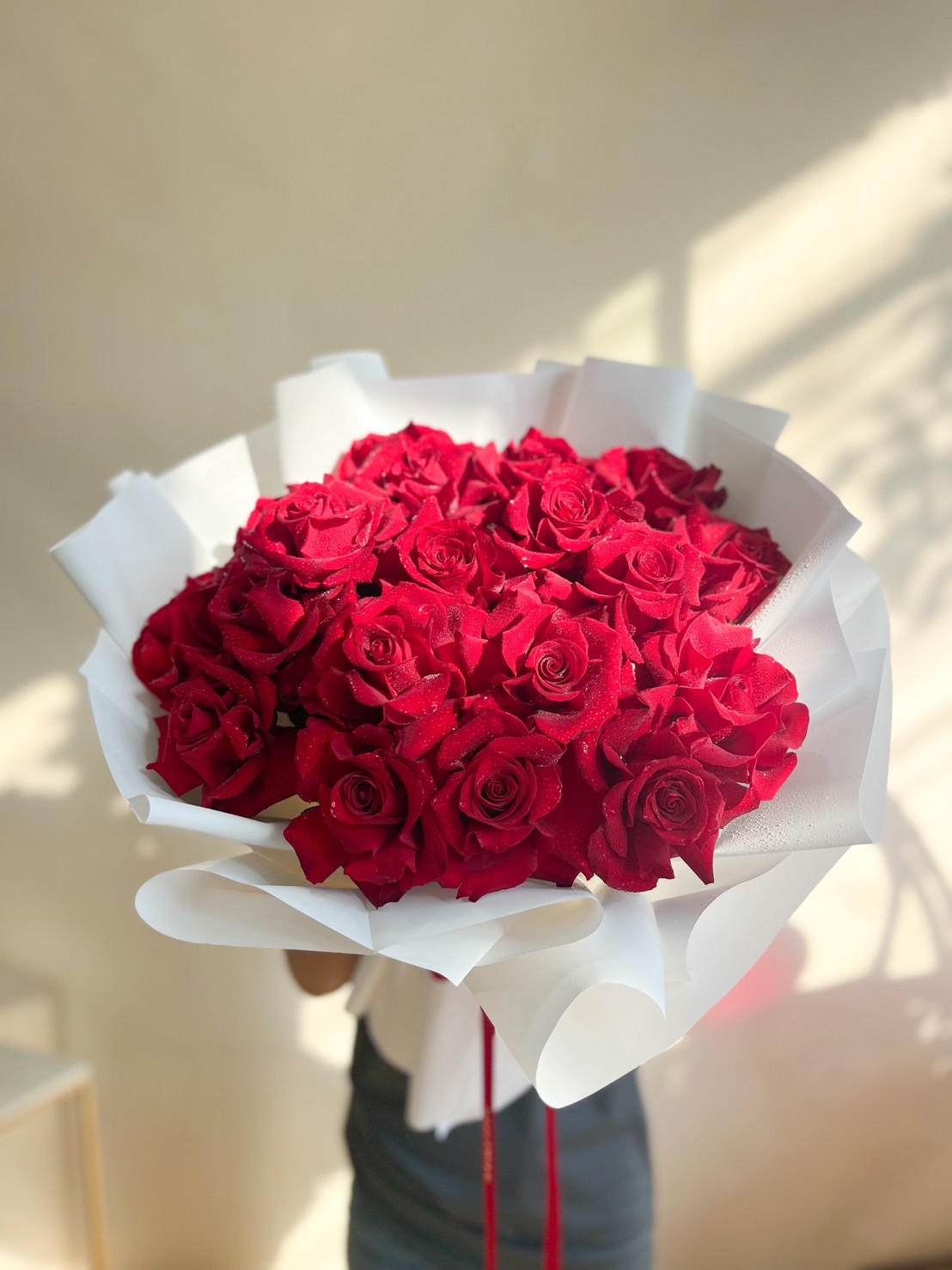 A stunning bouquet of red roses, elegantly wrapped in voluminous white paper with flowing ribbons for a sophisticated and romantic floral arrangement.