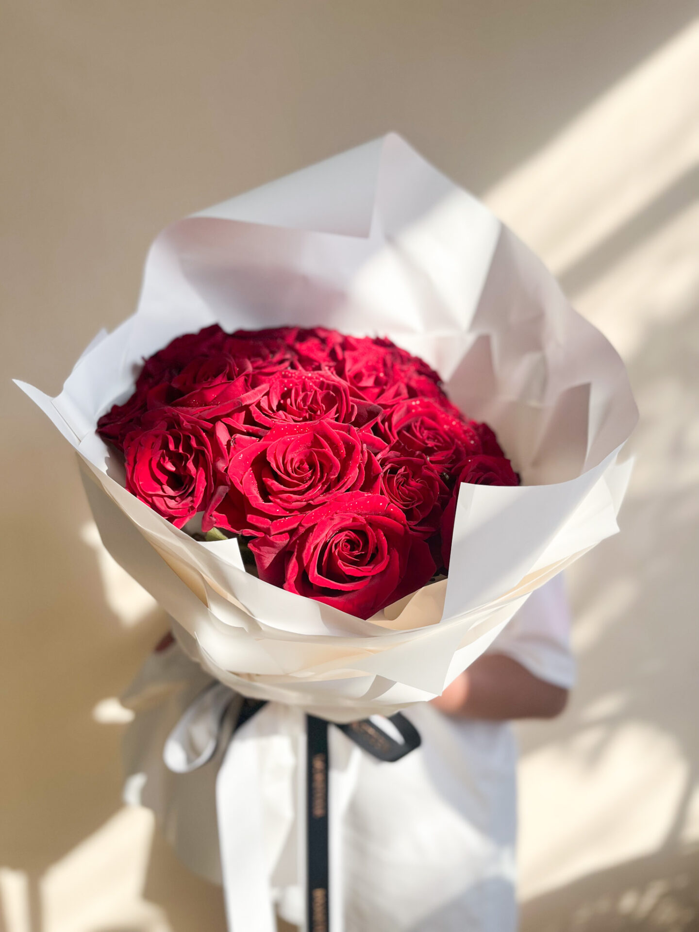 A stunning bouquet of red roses, elegantly wrapped in voluminous white paper with flowing ribbons for a sophisticated and romantic floral arrangement.