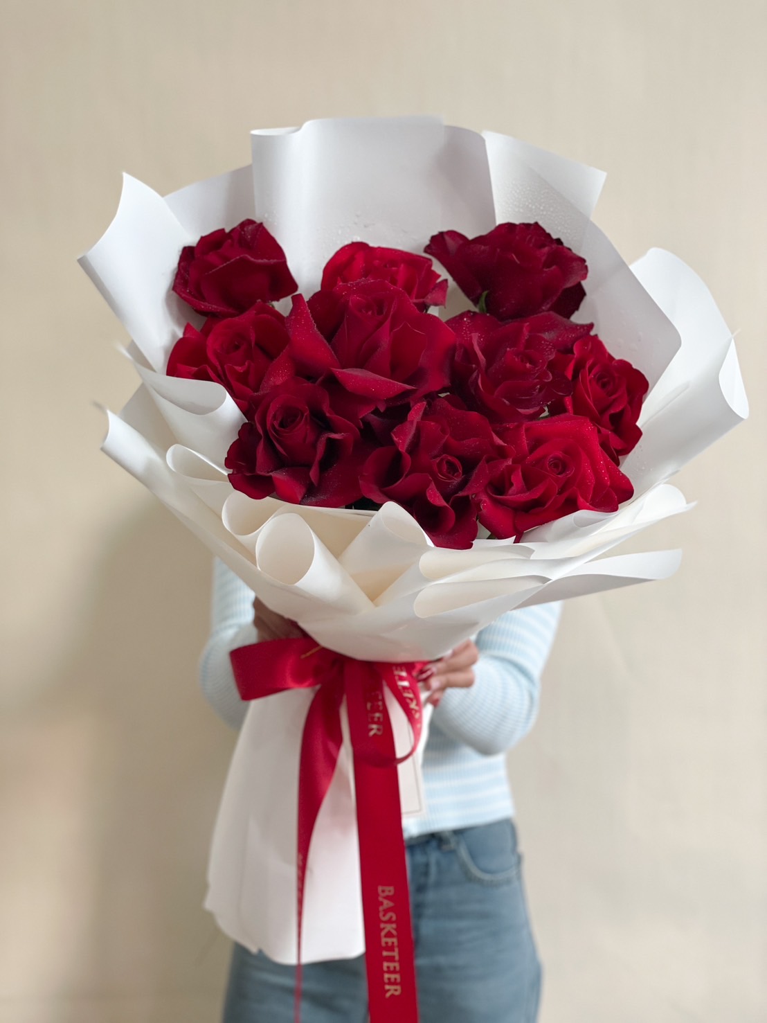 A stunning bouquet of red roses, elegantly wrapped in voluminous white paper with flowing ribbons for a sophisticated and romantic floral arrangement.