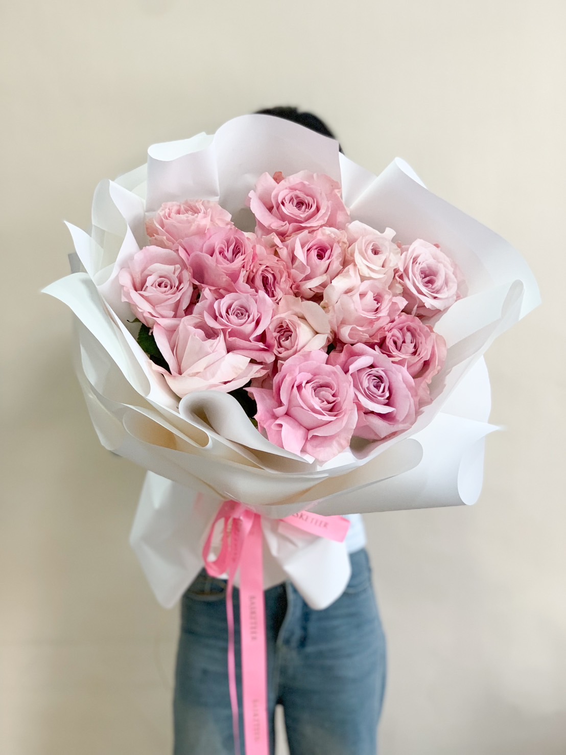 A luxurious bouquet of soft pink roses, wrapped in white with a pink satin ribbon, ideal for romantic gifts and special occasions.