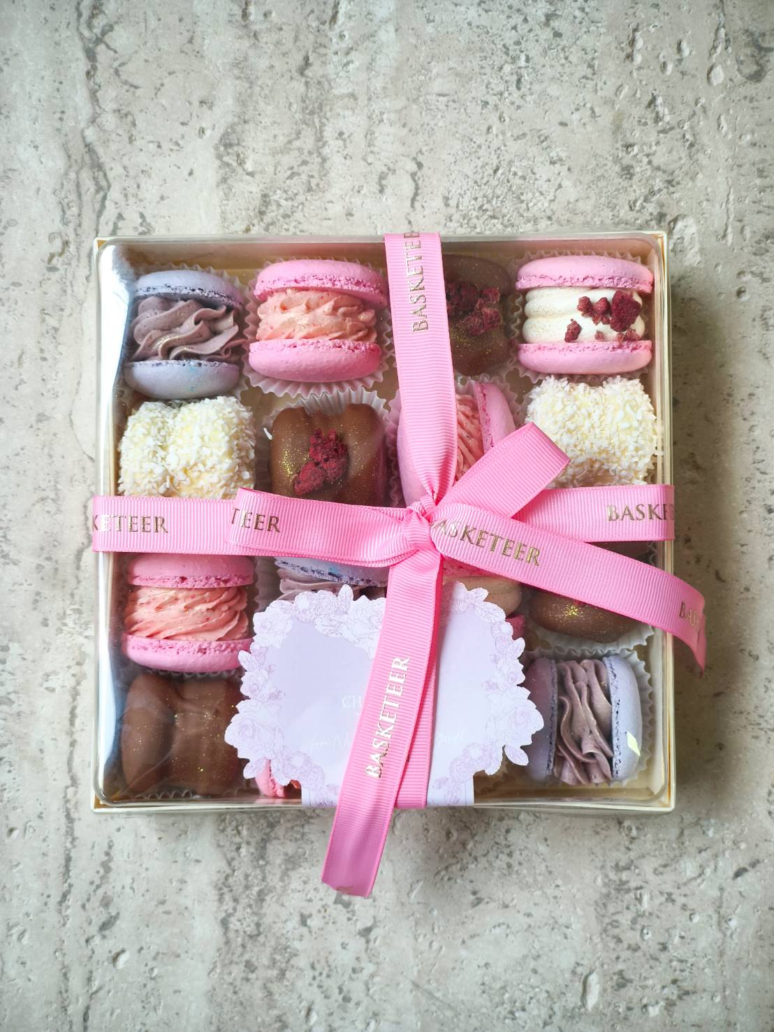 Premium dessert gift box with pink macarons, chocolate treats, and assorted sweets, tied with a pink satin ribbon.