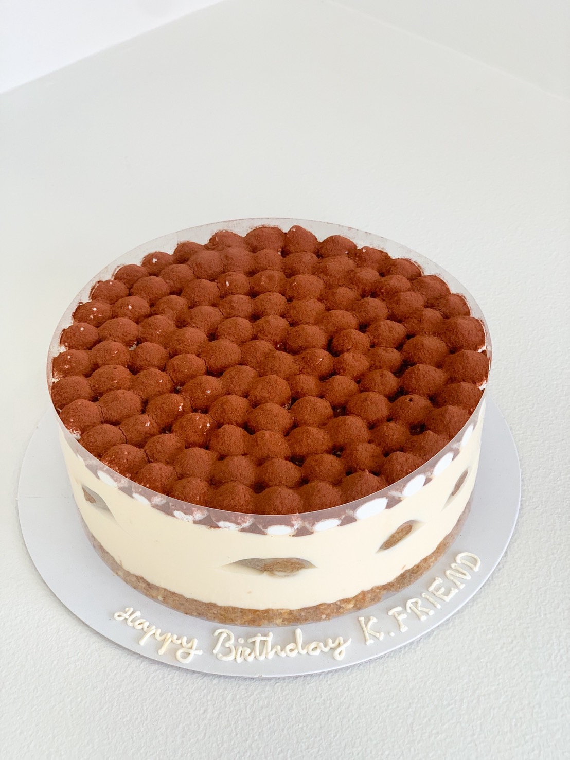 Classic tiramisu birthday cake with cocoa dusting and creamy mascarpone layers on a white cake board.