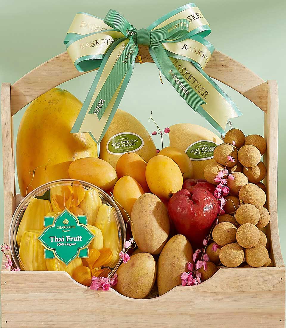An elegant Tropical Fusion Gift Basket filled with an assortment of tropical fruits including papaya, mangoes, rambutans, and longans, along with a plastic container of organic jackfruit pieces. The wooden basket is adorned with green and yellow ribbons and the text 