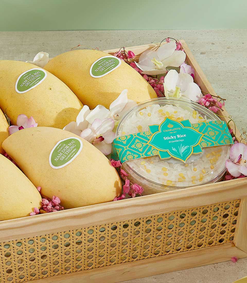 A woven basket containing four yellow mangoes with green stickers that read 