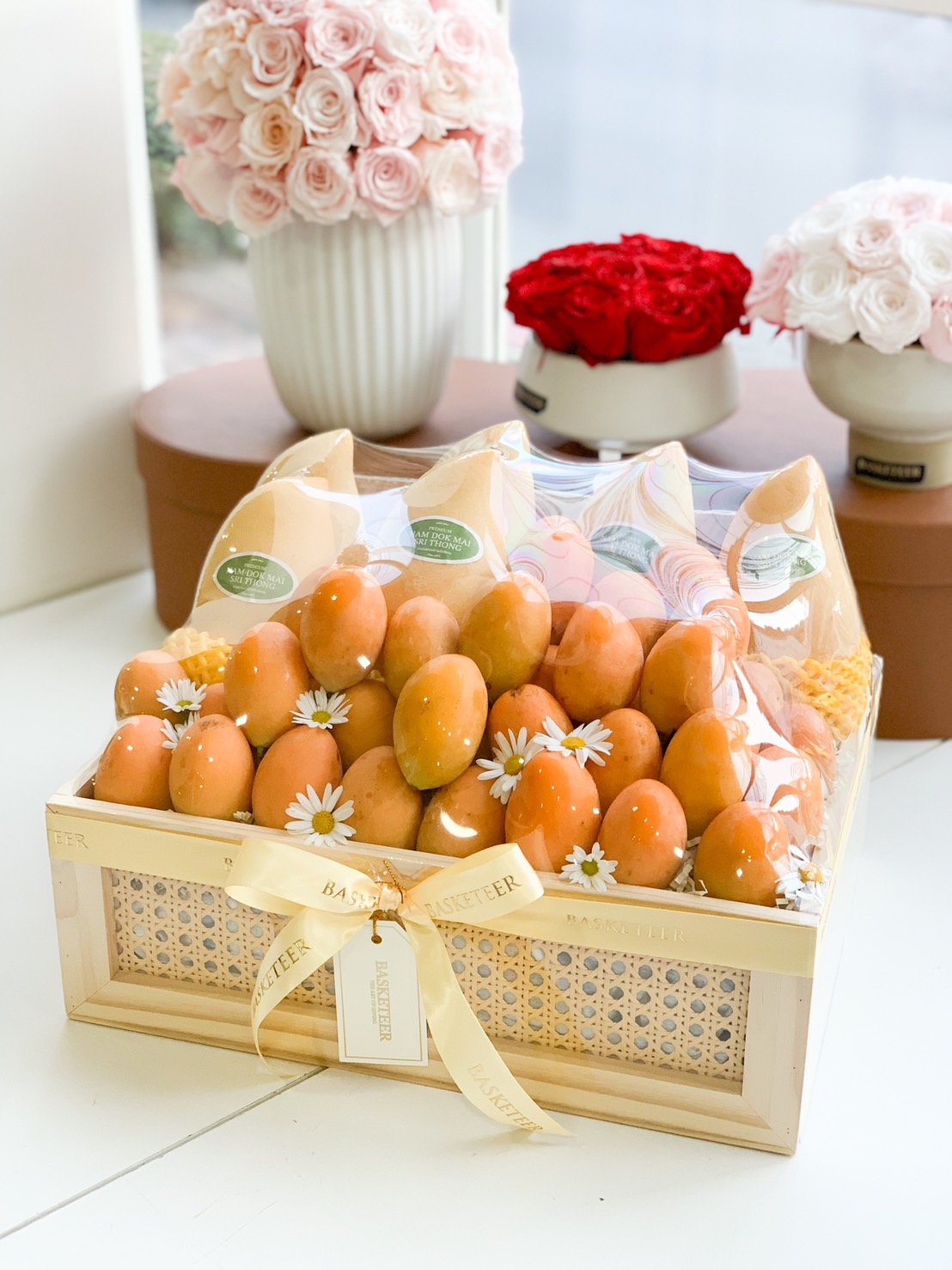 A luxurious fruit gift basket featuring premium Mayongchid (Marian Plum) and Nam Dok Mai See Thong mangoes, elegantly arranged in a handcrafted wooden crate with delicate floral decorations. Wrapped with a golden ribbon and a personalized Basketeer tag, this exquisite fruit box makes for a perfect luxury gift for any occasion.