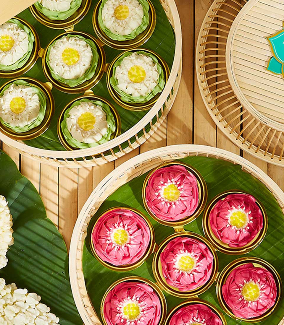 Top view of decorative arrangements of flowers in baskets with lids, reminiscent of Summertime Lotus Treats Gift. Each basket has flowers in different colors, including white, green, and pink, set on green leaf bases. The aesthetically arranged baskets are placed on a wooden surface for a pleasing visual.