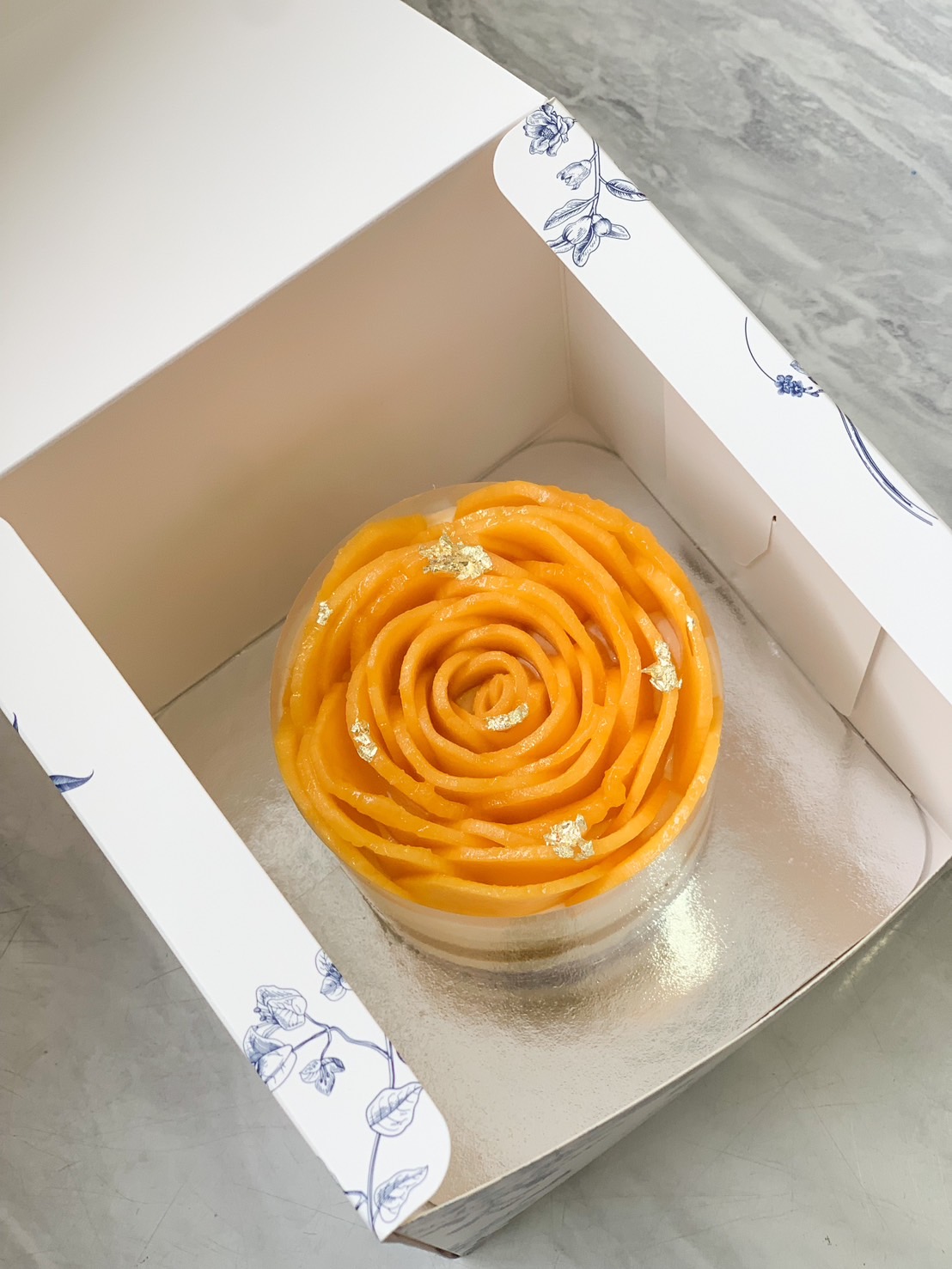A beautifully crafted mango cheesecake, designed with fresh mango slices arranged in a delicate rose pattern, adorned with edible gold flakes.