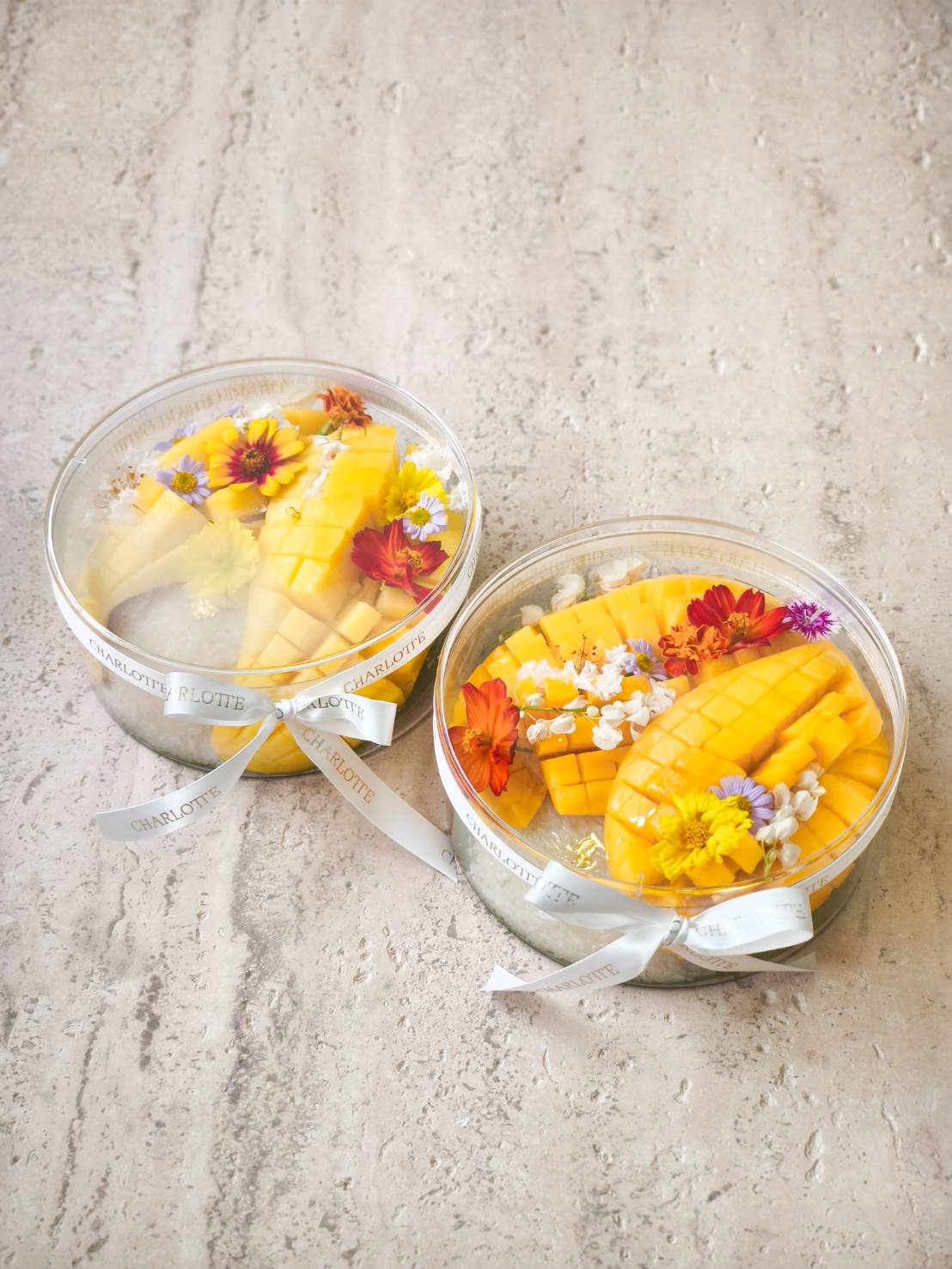Exquisite round Charlotte hampers with mango slices, adorned with vibrant edible flowers and white ribbons, crafted in Bangkok.