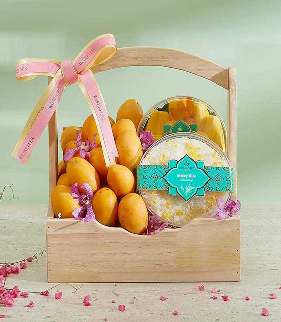 A gift basket featuring ripe yellow mayongchid and a serving of traditional sticky rice. The wooden basket is elegantly tied with a pink and yellow ribbon and adorned with delicate purple orchids.