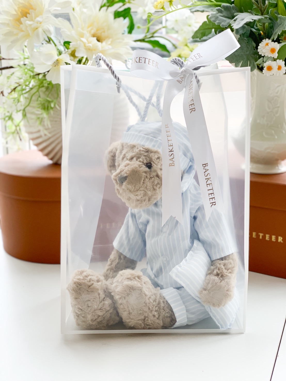 Cute teddy bear in blue pyjamas gift bag with white ribbon.