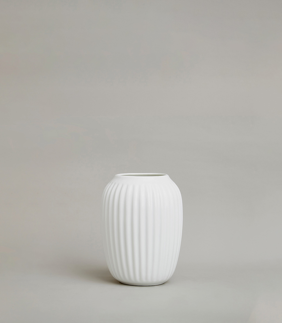 Minimalist white ceramic vase with a ribbed texture and oval shape, placed on a light grey background