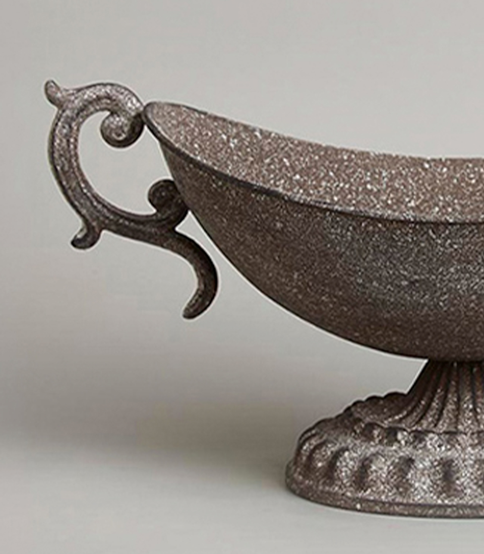 Close-up of an antique-style brown metal vase with intricate handles and a pedestal base.