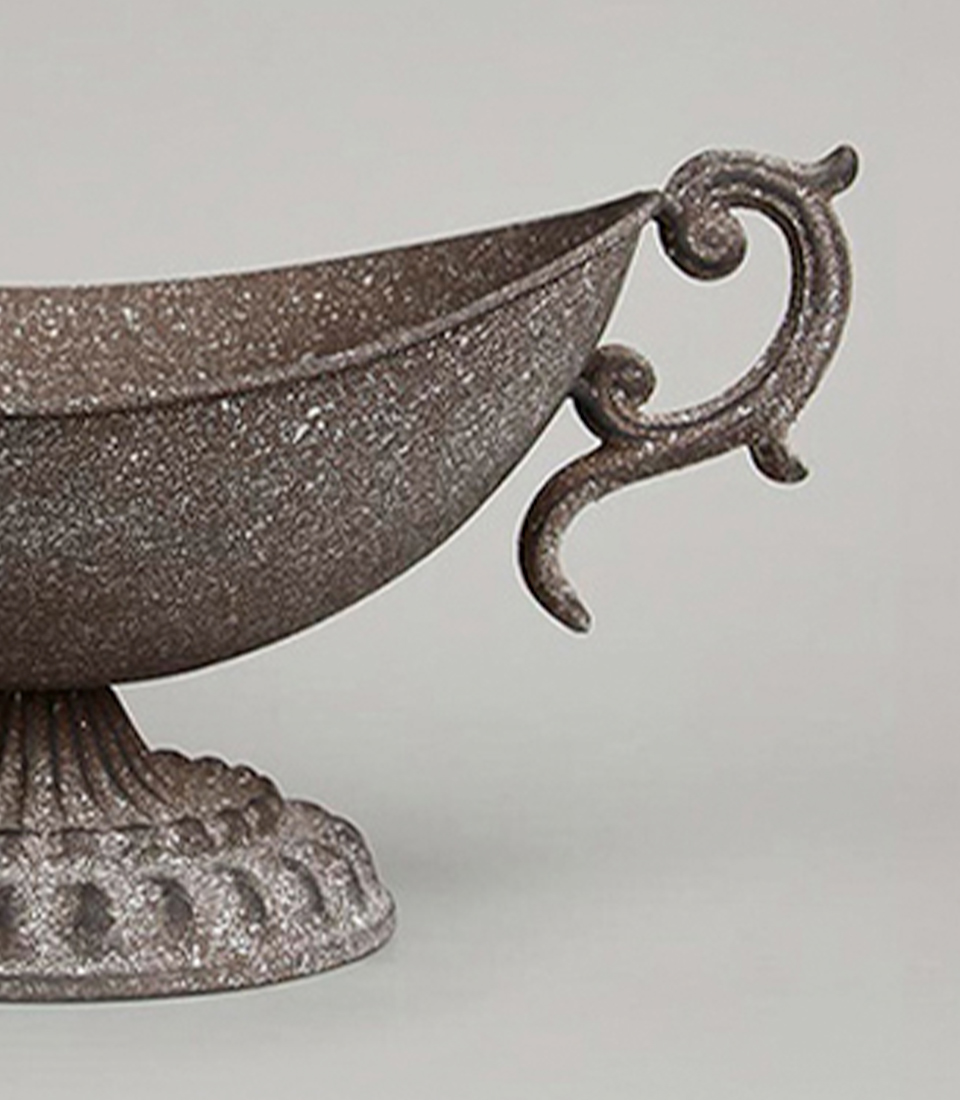 Close-up of an antique-style brown metal vase with intricate handles and a pedestal base.